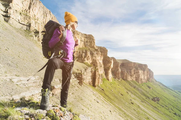 Lány turisztikai napszemüveg hozza egy hátizsák, a természet, a háttérben a felkészülés trekking hegymászás epikus sziklák — Stock Fotó