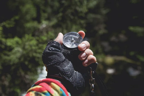 Een gehandschoende hand houdt een magnetisch kompas tegen de achtergrond van een naaldhout bos. Het concept van outdoor navigatie — Stockfoto