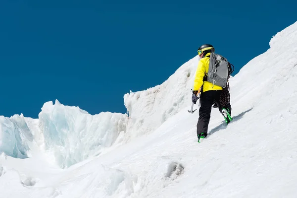 Uno sciatore in casco e maschera con uno zaino si erge su un pendio sullo sfondo di neve e una piccozza di ghiacciaio whith in mano. Backcountry Freeride — Foto Stock