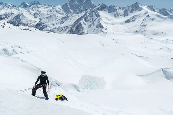 Um montanhista profissional em um capacete e máscara de esqui no seguro não entalhe o machado de gelo na geleira. O trabalho de um alpinista profissional no inverno em uma geleira contra o céu azul — Fotografia de Stock