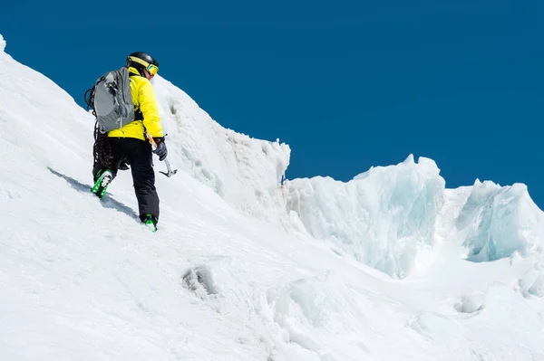 Bir kayakçı bir kask ve bir sırt çantası ile maske kar ve buzul whith buz baltası elinizle arka planı bir yamaç üzerinde yükselir. Backcountry Freeride — Stok fotoğraf