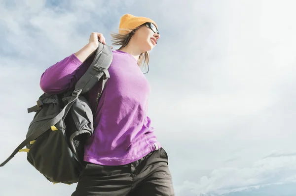 La muchacha de los turistas en las gafas de sol se pone la mochila al fondo del cielo de tarde. preparándose para el trekking con escalada. Ángulo ancho — Foto de Stock