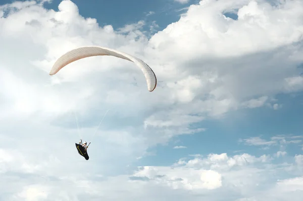 Profi-Gleitschirmflieger fliegt mit einem weißen Gleitschirm gegen den blauen Himmel und die weißen Wolken. Gleitschirmsport — Stockfoto