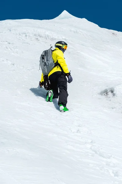 Ένας σκιέρ σε ένα κράνος και τη μάσκα με ένα σακίδιο υψώνεται σε μια πλαγιά με φόντο το χιόνι και ένα παγετώνα. Backcountry Freeride — Φωτογραφία Αρχείου