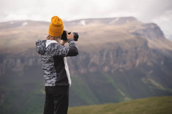 Una joven toma fotos de una meseta en la cima de una alta montaña en un día nublado. Vista de la chica detrás — Foto de Stock