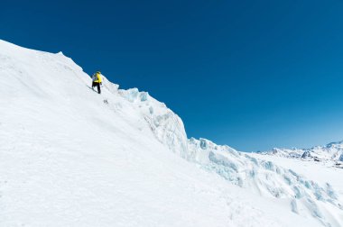 Bir kayakçı bir kask ve bir sırt çantası ile maske kar ve buzul whith buz baltası elinizle arka planı bir yamaç üzerinde yükselir. Backcountry Freeride