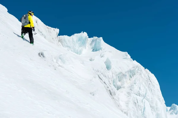 Un esquiador con casco y máscara con una mochila se levanta en una pendiente sobre el fondo de la nieve y un glaciar con hacha de hielo en la mano. Backcountry Freeride — Foto de Stock