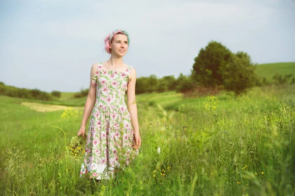 bir buket ile alaca elbiseli Genç mutlu gülümseyen kız olan yeşil çimen ülke yol boyunca yürüyüş