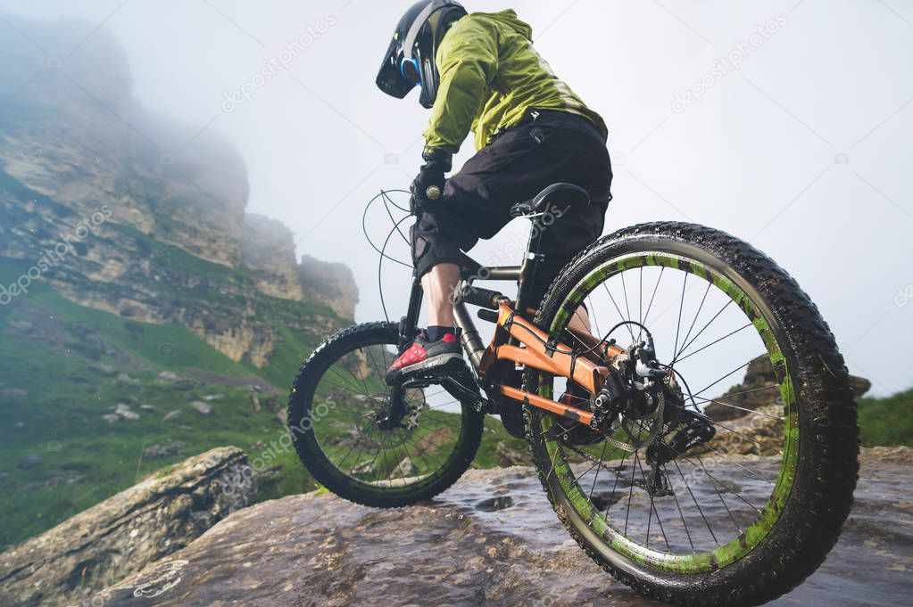 Legs of bicyclist and rear wheel close-up view of back mtb bike in mountains against background of rocks in foggy weather. The concept of extreme sports