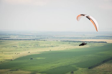 Bir koza arka planı, gökyüzü ve bulutlar bir yamaçparaşütü ile beyaz turuncu paraglide. Yamaç paraşütü spor