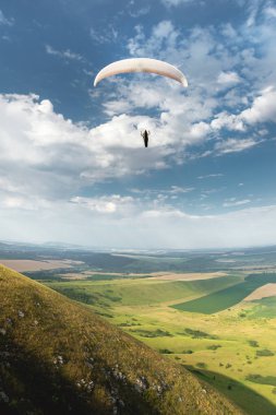 Bir koza arka planı, gökyüzü ve bulutlar bir yamaçparaşütü ile beyaz turuncu paraglide. Yamaç paraşütü spor