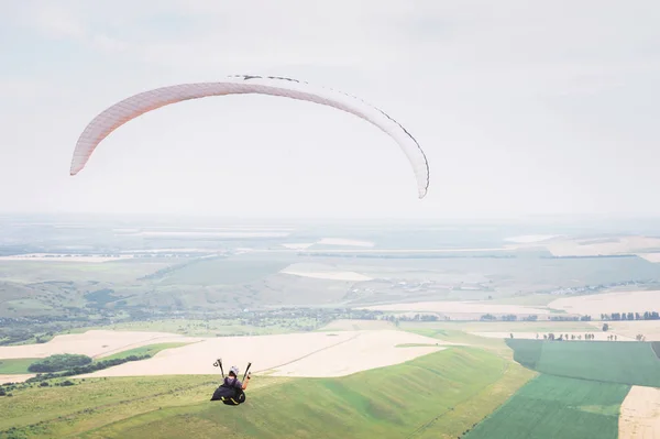 White orange paraglide with a paraglider in a cocoon against the background of fields of the sky and clouds. Paragliding Sports — Stock Photo, Image