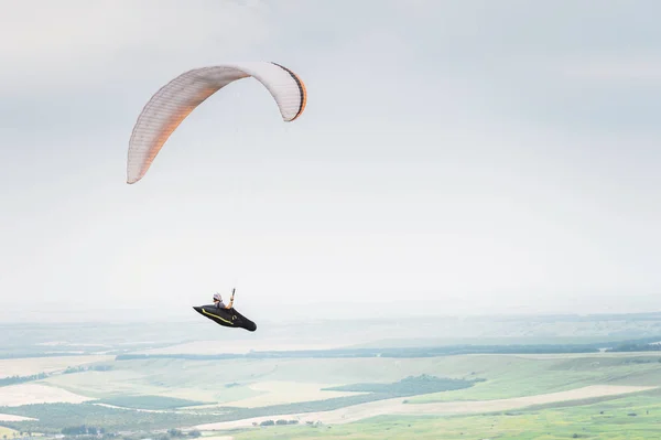 Parapente laranja branco com um parapente em um casulo contra o fundo dos campos do céu e nuvens. Parapente Esportes — Fotografia de Stock