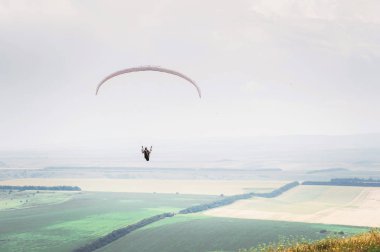 Bir koza arka planı, gökyüzü ve bulutlar bir yamaçparaşütü ile beyaz turuncu paraglide. Yamaç paraşütü spor