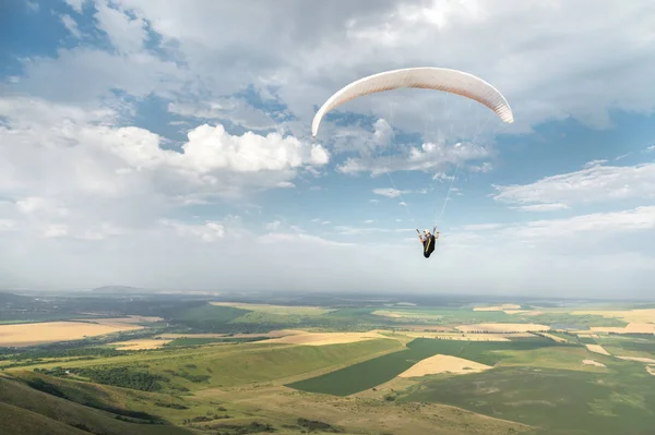 Weiße orange Gleitschirm mit einem Gleitschirm in einem Kokon vor dem Hintergrund der Felder des Himmels und Wolken. Gleitschirmsport — Stockfoto