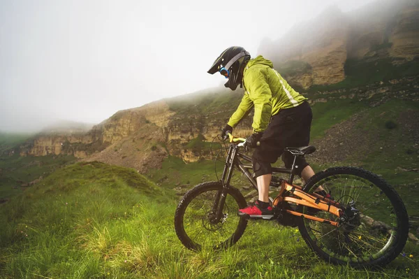 Un hombre en un casco de montaña montando una bicicleta de montaña pasea por la hermosa naturaleza en un clima nublado. cuesta abajo —  Fotos de Stock