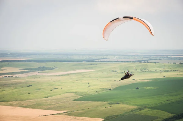 Parapente laranja branco com um parapente em um casulo contra o fundo dos campos do céu e nuvens. Parapente Esportes — Fotografia de Stock