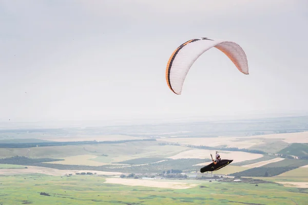 Parapente laranja branco com um parapente em um casulo contra o fundo dos campos do céu e nuvens. Parapente Esportes — Fotografia de Stock