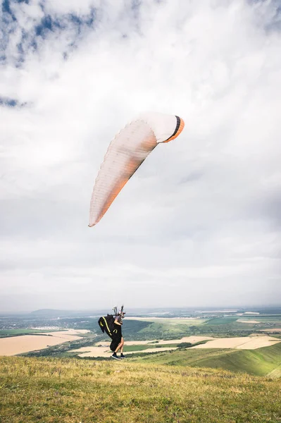 A man paraglider taking off from the edge of the mountain with fields in the background. Paragliding sports — Stock Photo, Image