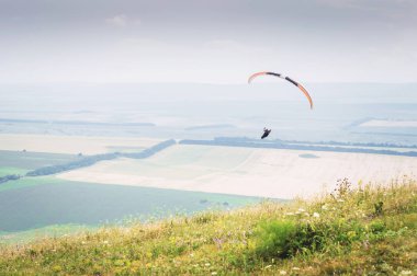 Bir koza arka planı, gökyüzü ve bulutlar bir yamaçparaşütü ile beyaz turuncu paraglide. Yamaç paraşütü spor