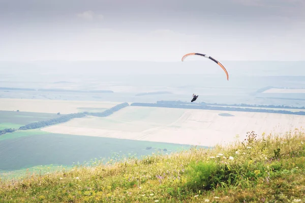 Parapente naranja blanco con un parapente en un capullo sobre el fondo de los campos del cielo y las nubes. Deportes de Parapente — Foto de Stock