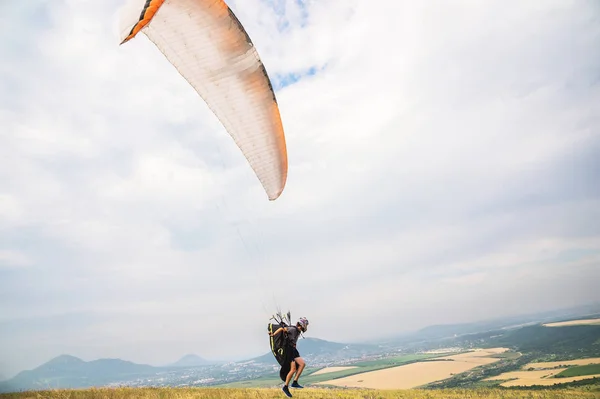A man paraglider taking off from the edge of the mountain with fields in the background. Paragliding sports — Stock Photo, Image