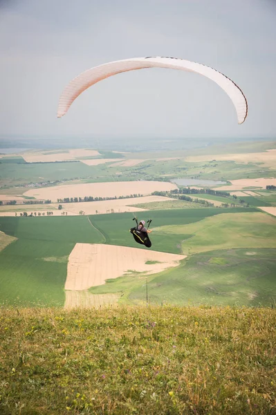 Weiße orange Gleitschirm mit einem Gleitschirm in einem Kokon vor dem Hintergrund der Felder des Himmels und Wolken. Gleitschirmsport — Stockfoto