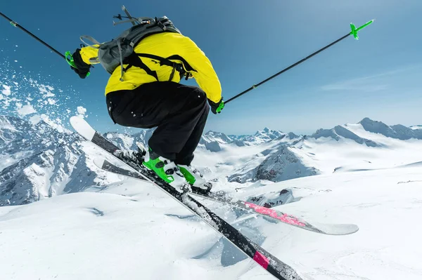 Um esquiador em equipamento desportivo completo salta para o abismo do topo da geleira contra o fundo do céu azul e as montanhas cobertas de neve caucasianas. Vista pelas traseiras. Região de Elbrus — Fotografia de Stock