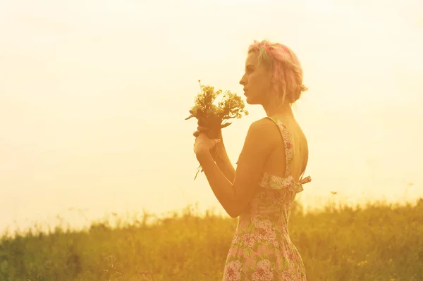 Mujer joven en vestido con ramo de flores en las manos al atardecer en el campo. Imagen tibia teñida — Foto de Stock