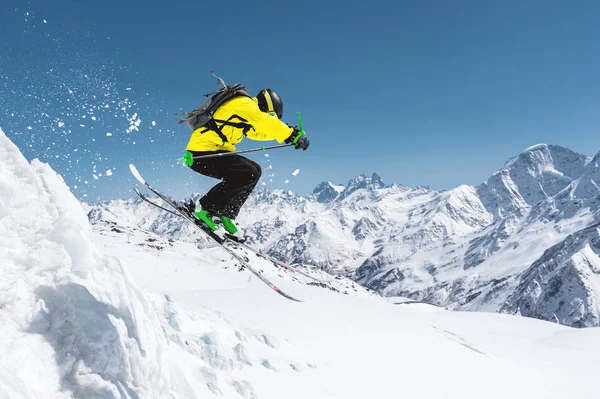 Vor dem Hintergrund des blauen Himmels und der kaukasischen schneebedeckten Berge springt ein Skifahrer in voller Sportausrüstung vom Gipfel des Gletschers in den Abgrund. elbrus region. Russland — Stockfoto