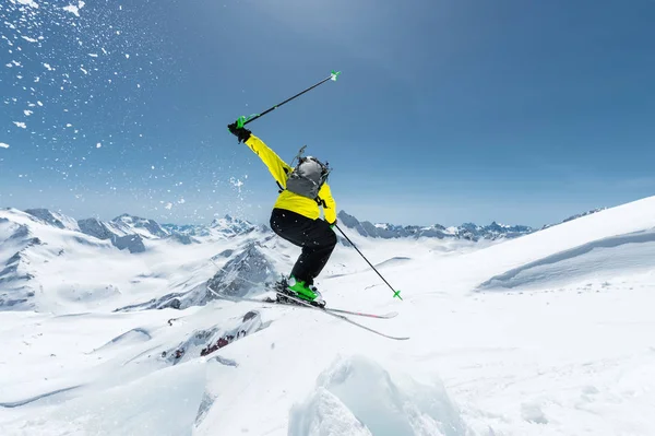 Un esquiador con equipamiento deportivo completo salta al abismo desde la cima del glaciar contra el fondo del cielo azul y las montañas caucásicas cubiertas de nieve. Vista desde atrás. Región de Elbrus —  Fotos de Stock