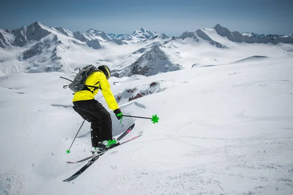 Uno sciatore in pieno equipaggiamento sportivo salta nell'abisso dalla cima del ghiacciaio sullo sfondo del cielo azzurro e delle montagne innevate caucasiche. Vista dal retro. Regione di Elbrus — Foto Stock