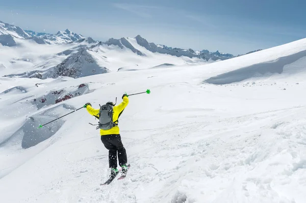 Tam bir kayakçı uçuruma ekipman atlar arka planı mavi gökyüzü ve Kafkas karla kaplı dağlar buzulun üstünden spor. Arkadan görüntüleyin. Elbrus bölge