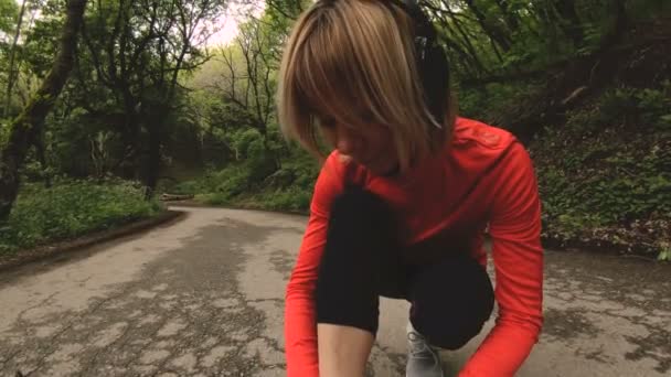 一个年轻的白种女孩坐在她的鞋带绑在在高加索的森林道路上慢跑之前。广角 — 图库视频影像