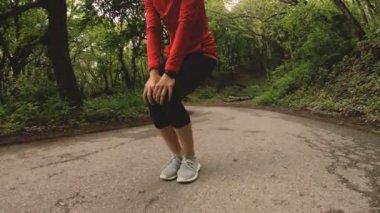 4 k genç sarışın bir kadın Kulaklığımda ormanda çalıştırmadan önce ısınma ve germe gerçekleştirir