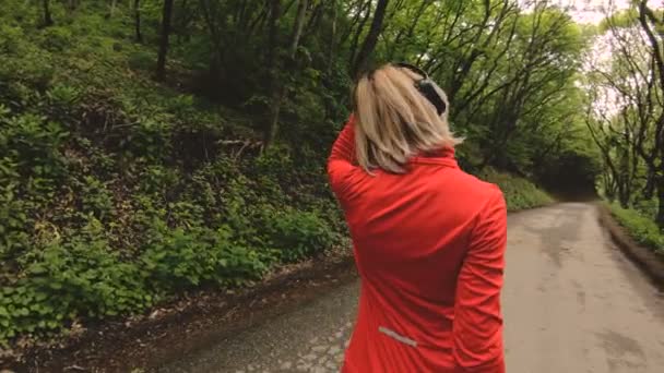 4k junge blonde Frau mit Kopfhörer macht Dehnen und Aufwärmen vor dem Laufen im Wald — Stockvideo