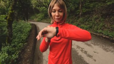 Genç çekici kadın kulaklık önünde akıllı izlemek veya yeşil orman yol koşu psole ayarlarını değiştirme