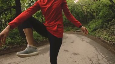 4 k genç sarışın bir kadın Kulaklığımda ormanda çalıştırmadan önce ısınma ve germe gerçekleştirir