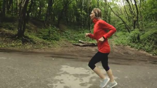 Chica corriendo. Chica rubia haciendo deportes al aire libre en el bosque de verano. Vista lateral de cámara lenta gran ángulo — Vídeos de Stock