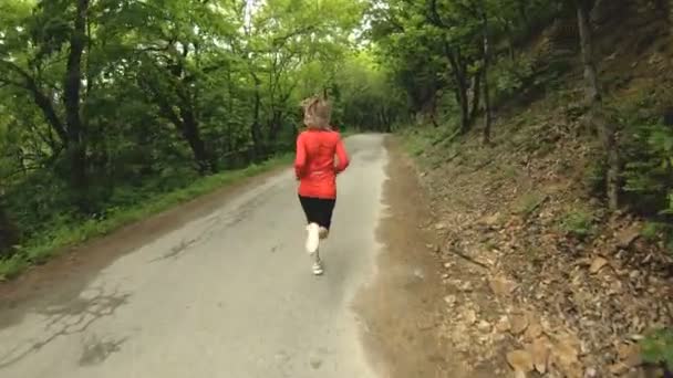 Fata care aleargă. Blonda face sporturi în aer liber în pădurea de vară. Vedere din spate unghi larg cu mișcare lentă — Videoclip de stoc