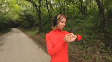 Genç çekici kadın kulaklık önünde akıllı izlemek veya yeşil orman yol koşu psole ayarlarını değiştirme
