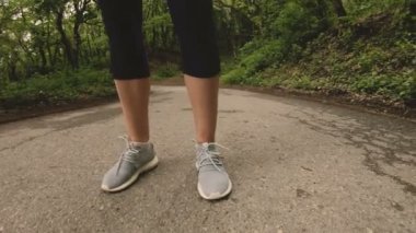4 k genç sarışın bir kadın Kulaklığımda ormanda çalıştırmadan önce ısınma ve germe gerçekleştirir