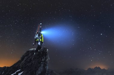 Gece manzarası. Bir sırt çantası ve kayaklar bir profesyonel backcountry kayakçı dağlarda bir kaya üzerinde duruyor ve far gökyüzüne parlar