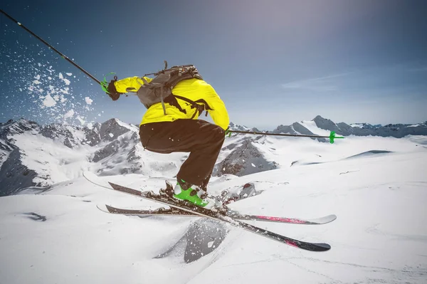 Lyžař v plné sportovní vybavení skočí do propasti z vrcholku ledovce na pozadí modré oblohy a kavkazských čepičkami. Pohled z zad. Elbrus region — Stock fotografie