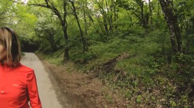 Genç çekici kadın kulaklık önünde akıllı izlemek veya yeşil orman yol koşu psole ayarlarını değiştirme.