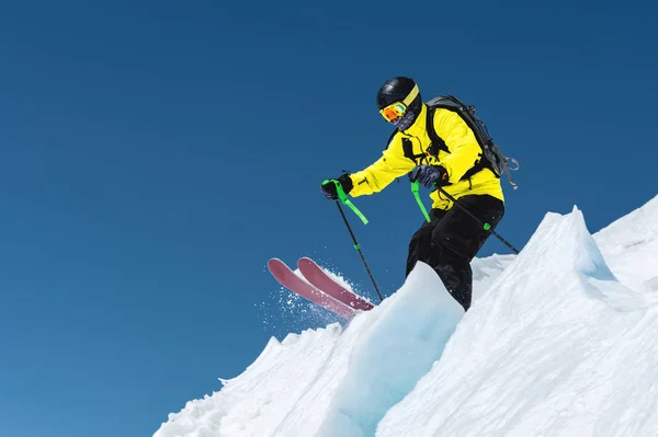 Vor dem Hintergrund des blauen Himmels und der kaukasischen schneebedeckten Berge springt ein Skifahrer in voller Sportausrüstung vom Gipfel des Gletschers in den Abgrund. elbrus region. Russland — Stockfoto