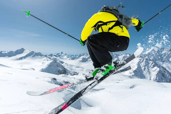 Un esquiador con equipamiento deportivo completo salta al abismo desde la cima del glaciar contra el fondo del cielo azul y las montañas caucásicas cubiertas de nieve. Vista desde atrás. Región de Elbrus —  Fotos de Stock