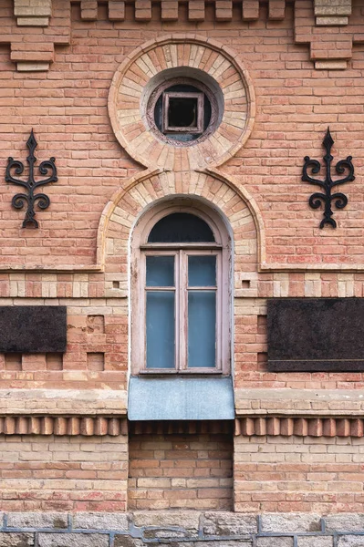 Vintage arched window in the wall of yellow brick. Black glass in a maroon dark red wooden frame. The concept of antique vintage architecture in building elements.