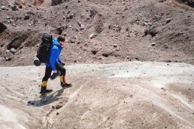 Bir sırt çantası ile bir dağcı çatlaklar dağ arasında elinde kaldırımlar ile tozlu bir buzul boyunca yürüyüş krampon içeri girer