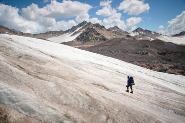 Bir sırt çantası ile bir dağcı çatlaklar dağ arasında elinde kaldırımlar ile tozlu bir buzul boyunca yürüyüş krampon içeri girer